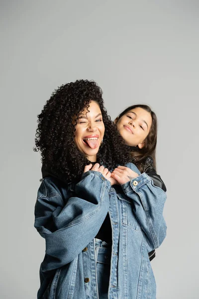Curly woman sticking out tongue near kid isolated on grey — стоковое фото