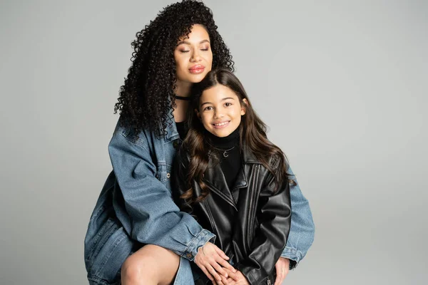 Young mother in denim jacket hugging smiling kid isolated on grey — Stock Photo