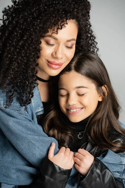 Portrait of smiling woman hugging child with closed eyes isolated on grey — Stock Photo