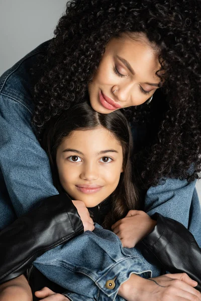 Stylish young woman hugging cheerful preteen daughter isolated on grey — Stockfoto