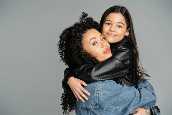 Positive preteen kid hugging mom in denim jacket isolated on grey — Stock Photo