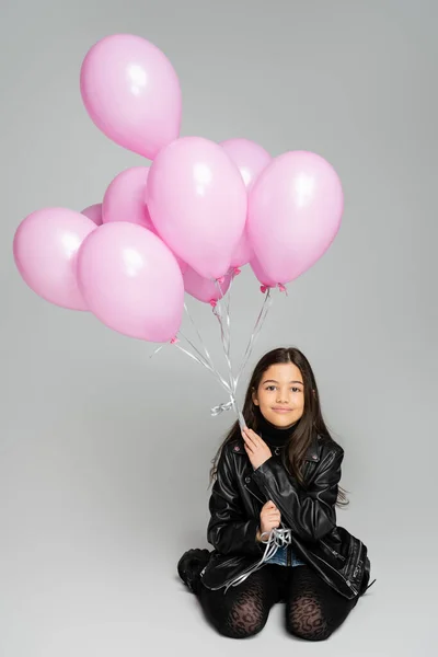 Elegante niño en chaqueta de cuero con globos rosados sobre fondo gris - foto de stock