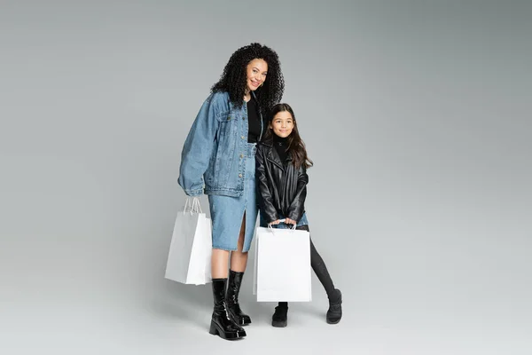 Madre y niño preadolescente de moda sosteniendo compras en un fondo gris - foto de stock