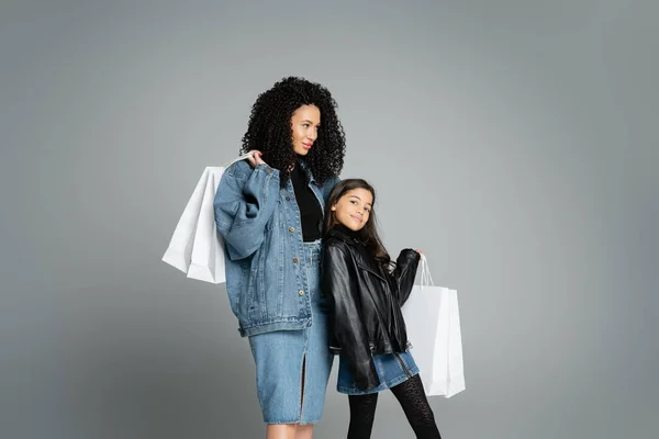 Trendy mother and daughter holding white shopping bags isolated on grey — Photo de stock