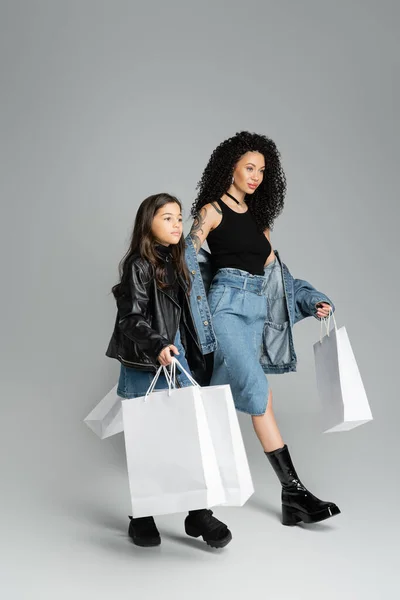 Trendige Mutter und Kind halten Einkaufstüten in der Hand und gehen auf grauem Hintergrund — Stockfoto