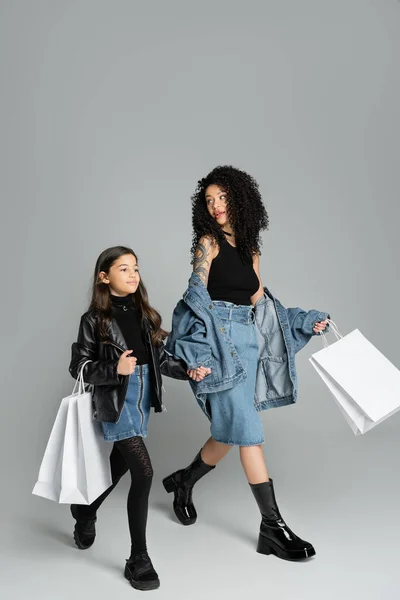 Trendy mom and daughter holding hands and shopping bags on grey background — Photo de stock