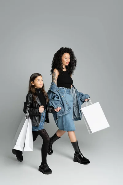 Preteen kid holding shopping bags and hand of stylish mom on grey background — Photo de stock