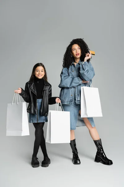 Stylish mother and daughter holding credit card and shopping bags on grey background — Stockfoto