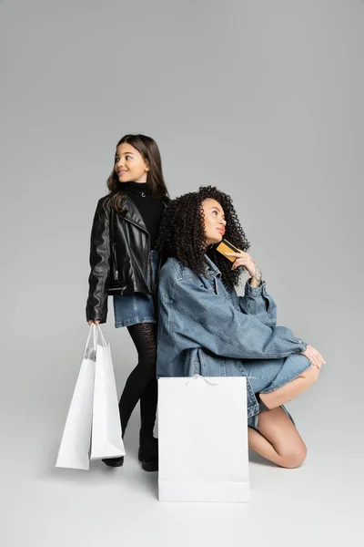 Positive Preteen Mädchen mit Einkaufstüten in der Nähe Mama mit Kreditkarte auf grauem Hintergrund — Stockfoto