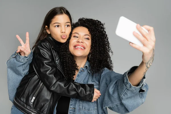 Stylish mother and daughter taking selfie on smartphone isolated on grey — Stock Photo
