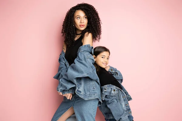 Trendy woman and child in denim jackets posing on pink background - foto de stock
