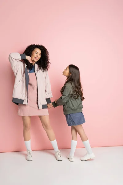 Stylish woman posing near daughter on pink background - foto de stock