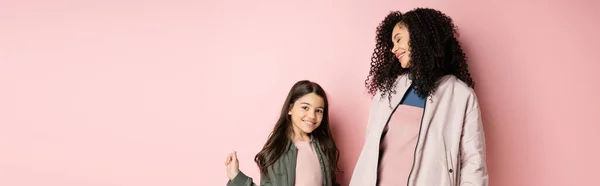 Donna riccia sorridente vicino figlia elegante su sfondo rosa, banner — Foto stock