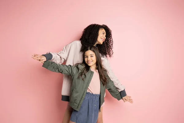 Smiling woman holding hands of preteen kid on pink background - foto de stock