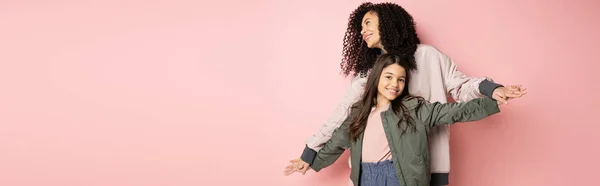 Stylish young woman holding hands of daughter on pink background, banner - foto de stock