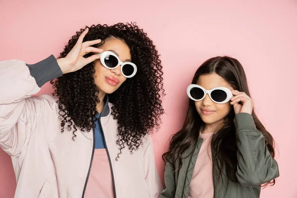 Stylish mother and daughter holding sunglasses on pink background - foto de stock