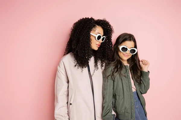 Donna e ragazza alla moda in occhiali da sole in piedi su sfondo rosa — Foto stock