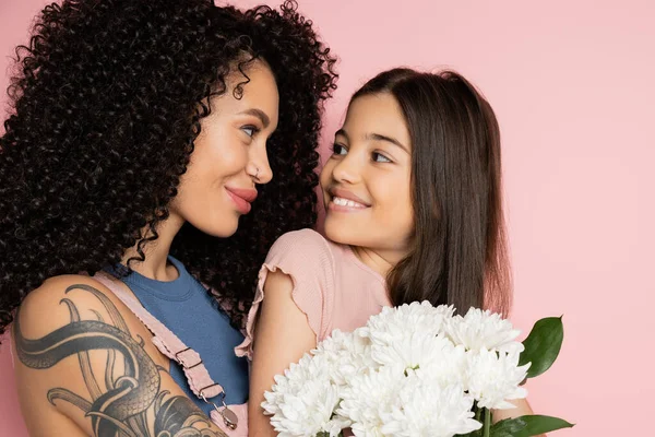 Preteen kid looking at stylish mom near bouquet on pink background — Stock Photo