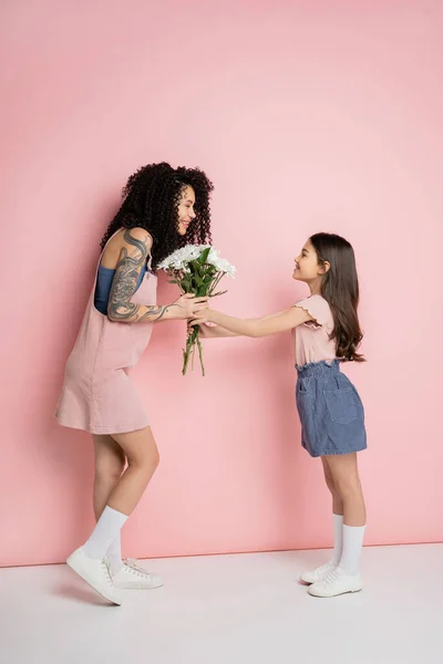 Side view of girl giving bouquet to trendy mother on pink background — Stock Photo