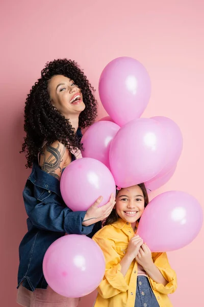 Excited woman standing near daughter and balloons on pink background — Stock Photo