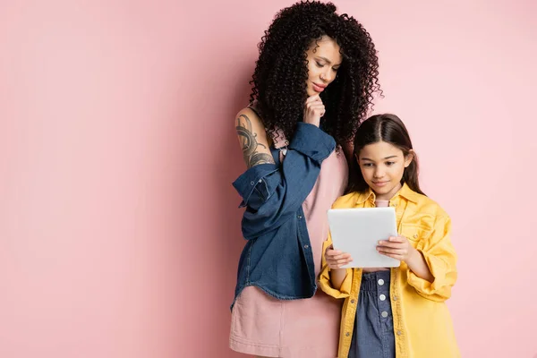 Pensive mother looking at digital tablet near daughter on pink background — Stock Photo