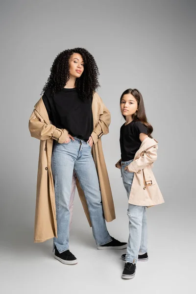 Preteen child in trench coat posing near stylish mom on grey background — Foto stock