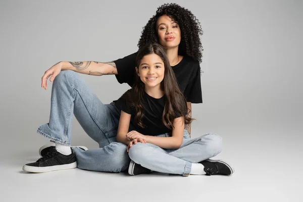 Niño y madre positivos en jeans y camisetas posando sobre fondo gris - foto de stock