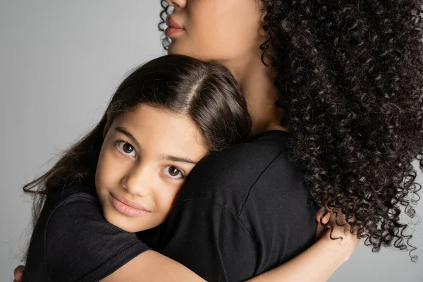 Portrait of preteen child hugging curly mom and looking at camera isolated on grey — Stock Photo