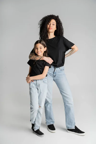 Stylish woman hugging preteen girl and posing on grey background — Photo de stock