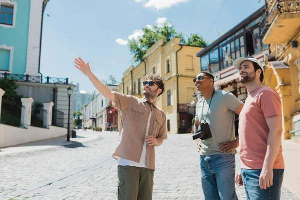 Екскурсовод у сонцезахисних окулярах, що вказують рукою під час екскурсії з міжрасовими туристами на спуску Ендрюса в Києві. — стокове фото