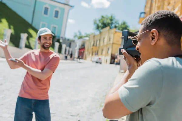 Африканский американец с винтажной камерой фотографирует счастливого туриста, указывающего руками на спуск Эндрюса в Киеве — стоковое фото
