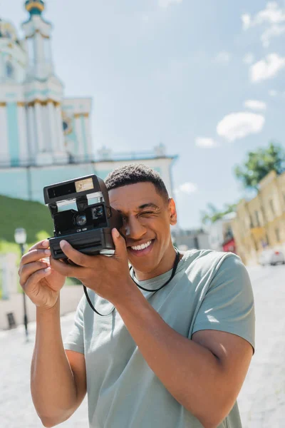 Cheerful african american tourist taking photo on vintage camera on Andrews descent in Kyiv, Ukraine — Stock Photo