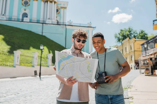 Guida turistica in occhiali da sole e viaggiatore afroamericano con fotocamera vintage guardando la mappa della città sulla discesa Andrews a Kiev, Ucraina — Foto stock