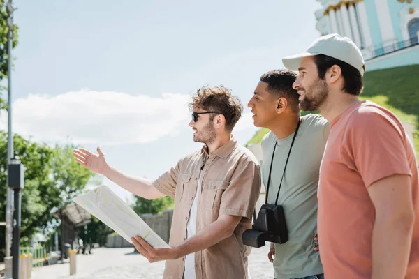 Side view of young guide with city map pointing with hand near multicultural travelers on Andrews descent in Kyiv — Stock Photo