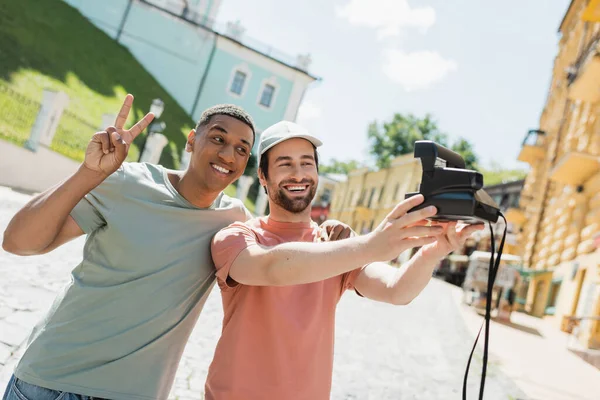 Uomo afroamericano sorridente mostrando segno di pace vicino amico barbuto prendere selfie sulla fotocamera vintage Andrews discesa a Kiev — Foto stock