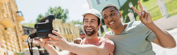Happy african american man showing victory sign near friend taking selfie on vintage camera on Andrews descent in Kyiv, banner — Stock Photo