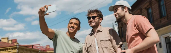 Happy african american traveler taking selfie with tour guide in sunglasses and bearded man on Andrews descent in Kyiv, banner — Stock Photo