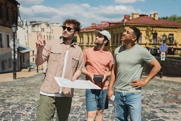 Екскурсовод у сонцезахисних окулярах, що тримають карту і вказують пальцем біля міжрасових мандрівників на спуск Ендрюса в Києві. — стокове фото