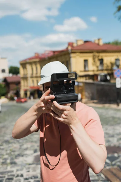Young man in sun cap taking photo on vintage camera on Andrews descent in Kyiv — Stock Photo