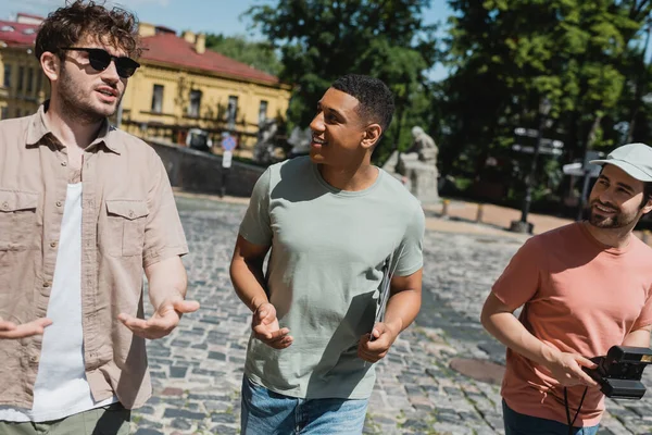 Uomini multietnici sorridenti che ascoltano giovani guide in occhiali da sole mentre camminano sulla discesa di Andrews a Kiev — Foto stock