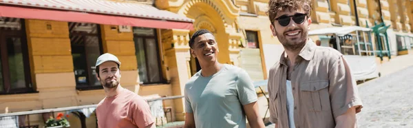 Young tour guide in sunglasses smiling during excursion with interracial tourists on Andrews descent in Kyiv, banner — Stock Photo