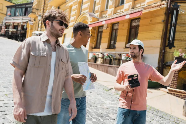 Bearded man with vintage camera pointing with hand near multicultural friends on Andrews descent in Kyiv — Stock Photo