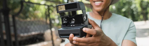 Vista parziale del viaggiatore afroamericano offuscato con fotocamera vintage che scatta foto nel parco, banner — Foto stock