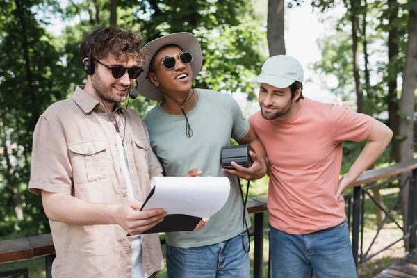 Amazed african american man with vintage camera looking away near tour guide holding clipboard in city park — Stock Photo