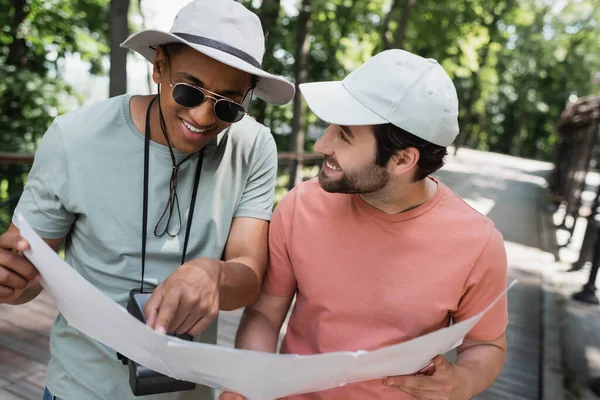 Lächelnder afrikanisch-amerikanischer Tourist mit Sonnenbrille zeigt auf Karte neben bärtigem Freund im Sommerpark — Stockfoto