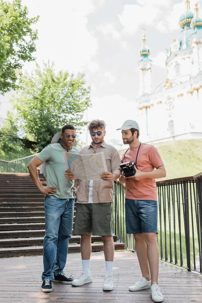 Interracial travelers with city map standing on stairs near St Andrews church on blurred background in Kyiv — Stock Photo