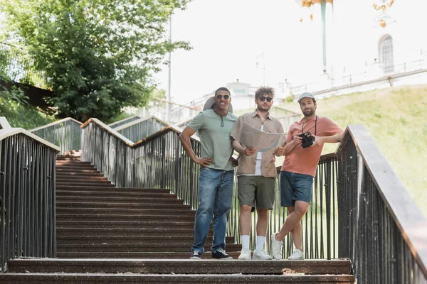 Полная длина счастливых межрасовых туристов с карты города стоя на лестнице в городе — стоковое фото