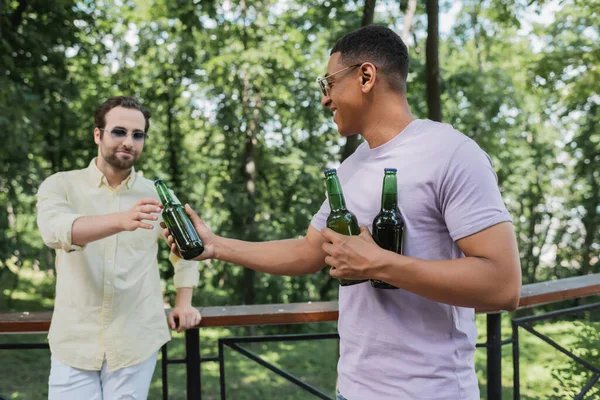 Carefree african american man giving bottle of beer to friend in city park — Stock Photo
