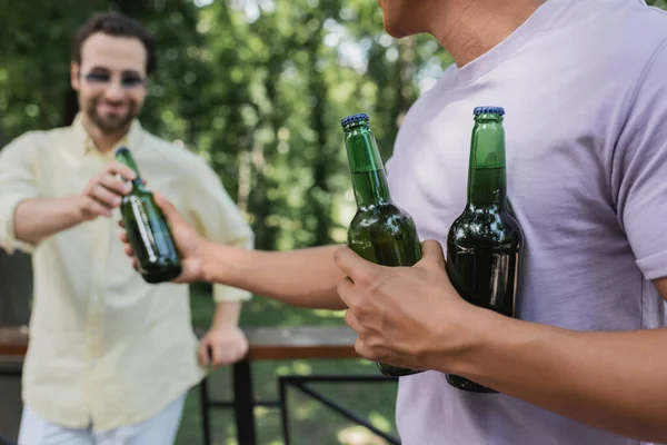 Africano americano hombre dando fresco cerveza a borrosa amigo en parque - foto de stock