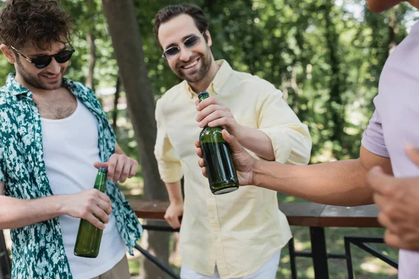 Amigos interracial despreocupados y elegantes sosteniendo botellas de cerveza fresca en el parque de verano - foto de stock